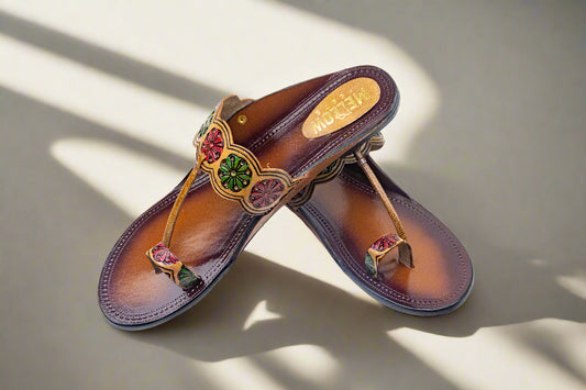 Pair of brown sandals with decorative straps and gemstones on a white background