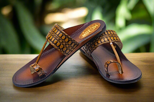 Pair of brown sandals with decorative straps on a wooden surface with a blurred green background