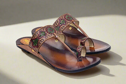 Elegant handcrafted leather flats with traditional hand-tooled floral patterns in red and green, featuring a classic toe loop design — artisanal ethnic footwear by Mellow Feets for festive and everyday style.