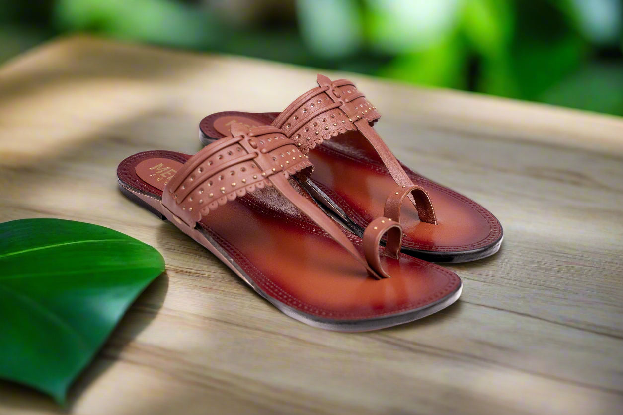 Pair of brown sandals on a wooden surface with a blurred green leaf in the background