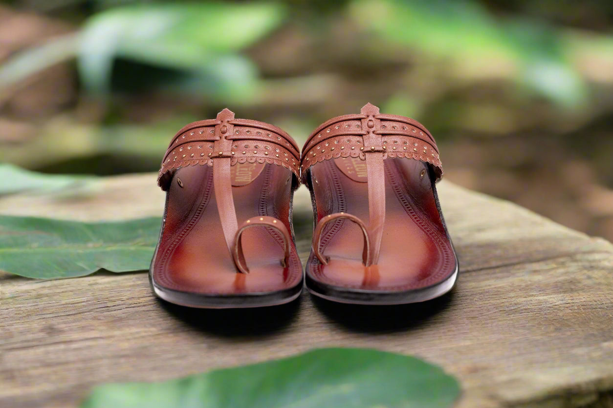 Pair of brown sandals on a wooden surface with green leaves in the background