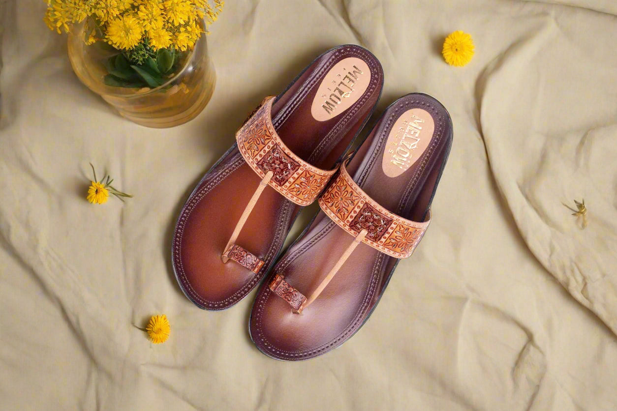 Pair of brown sandals with decorative straps on a beige fabric background with yellow flowers.