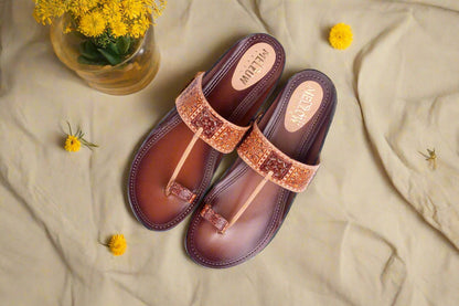 Pair of brown sandals with decorative straps on a beige fabric background with yellow flowers.