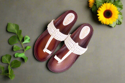 Pair of brown sandals with white straps on a gray background with green leaves and a sunflower.