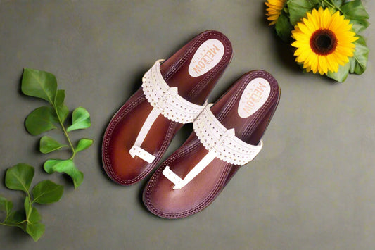 Pair of brown sandals with white straps on a gray background with green leaves and a sunflower.