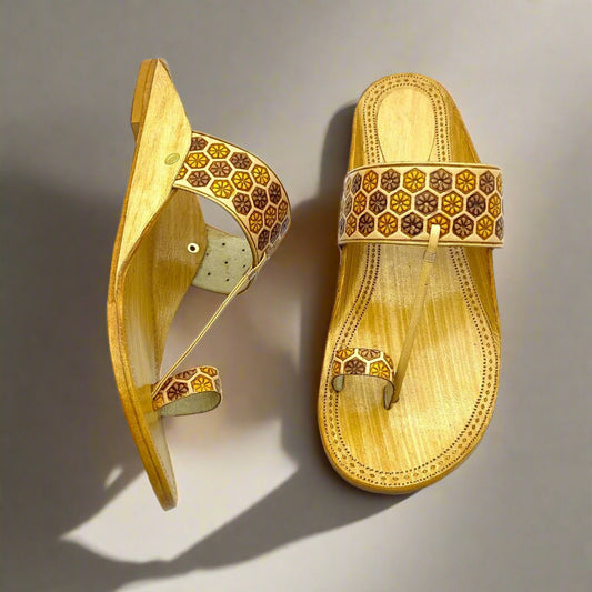 Traditional light tan kolhapuri sandals with hexagonal floral motifs in brown and yellow on the broad strap and toe loop.