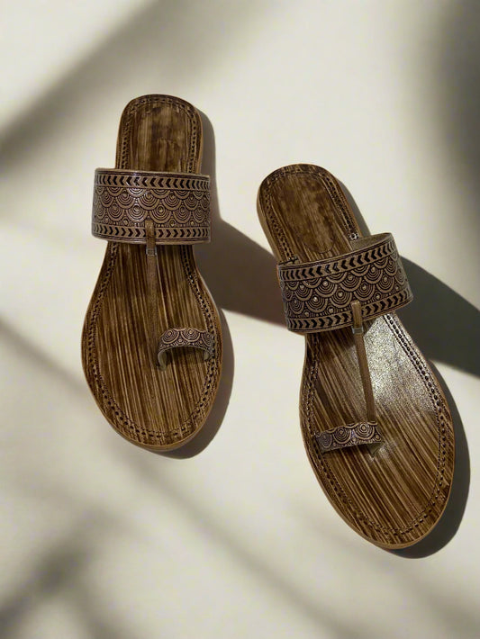 Handcrafted brown leather kolhapuri sandals featuring intricate carved patterns on the broad front strap and toe ring.
