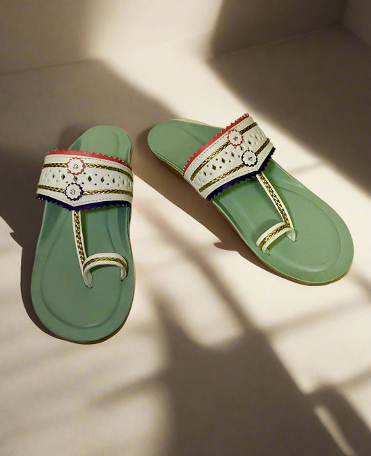 Pastel green handcrafted flats with white leather strap detailing, featuring gold braided accents and scalloped edges in red and purple, with small embroidered floral motifs.