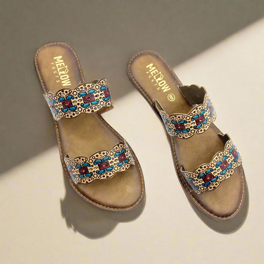 Handcrafted brown leather flats by Mellow Feets, featuring twin scalloped straps embroidered with intricate floral patterns in teal blue, maroon, and beige.