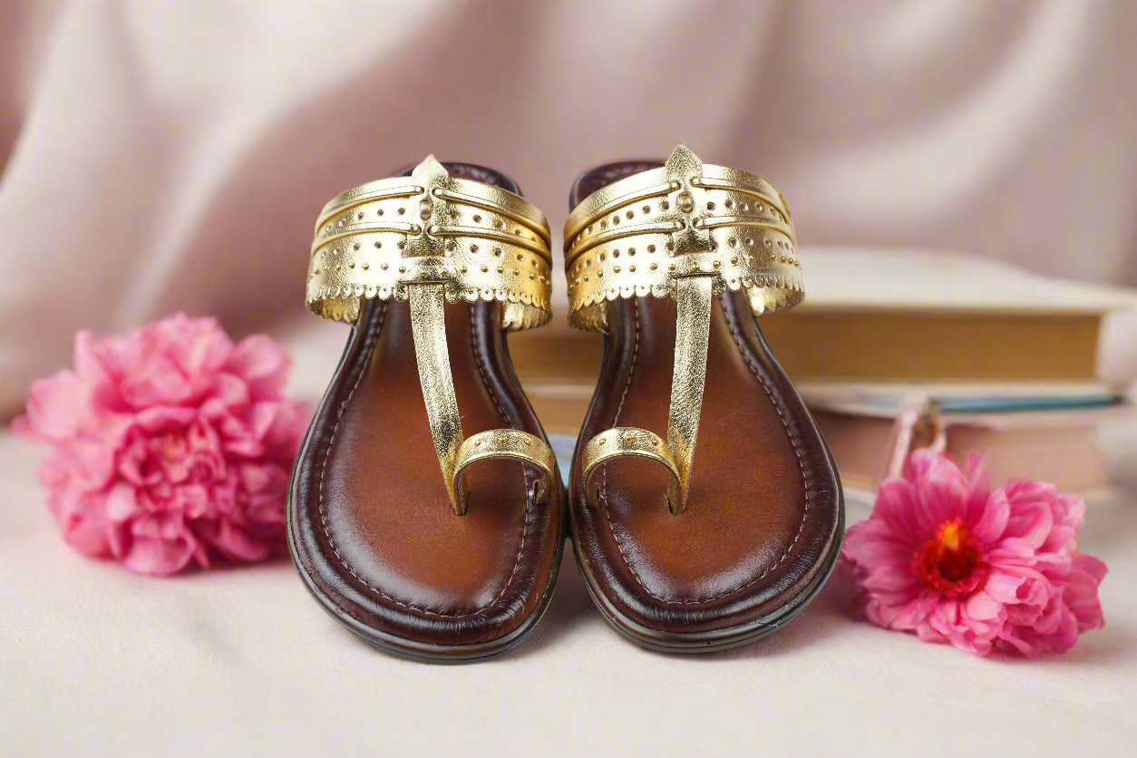 Pair of brown sandals with gold straps on a light background with pink flowers.
