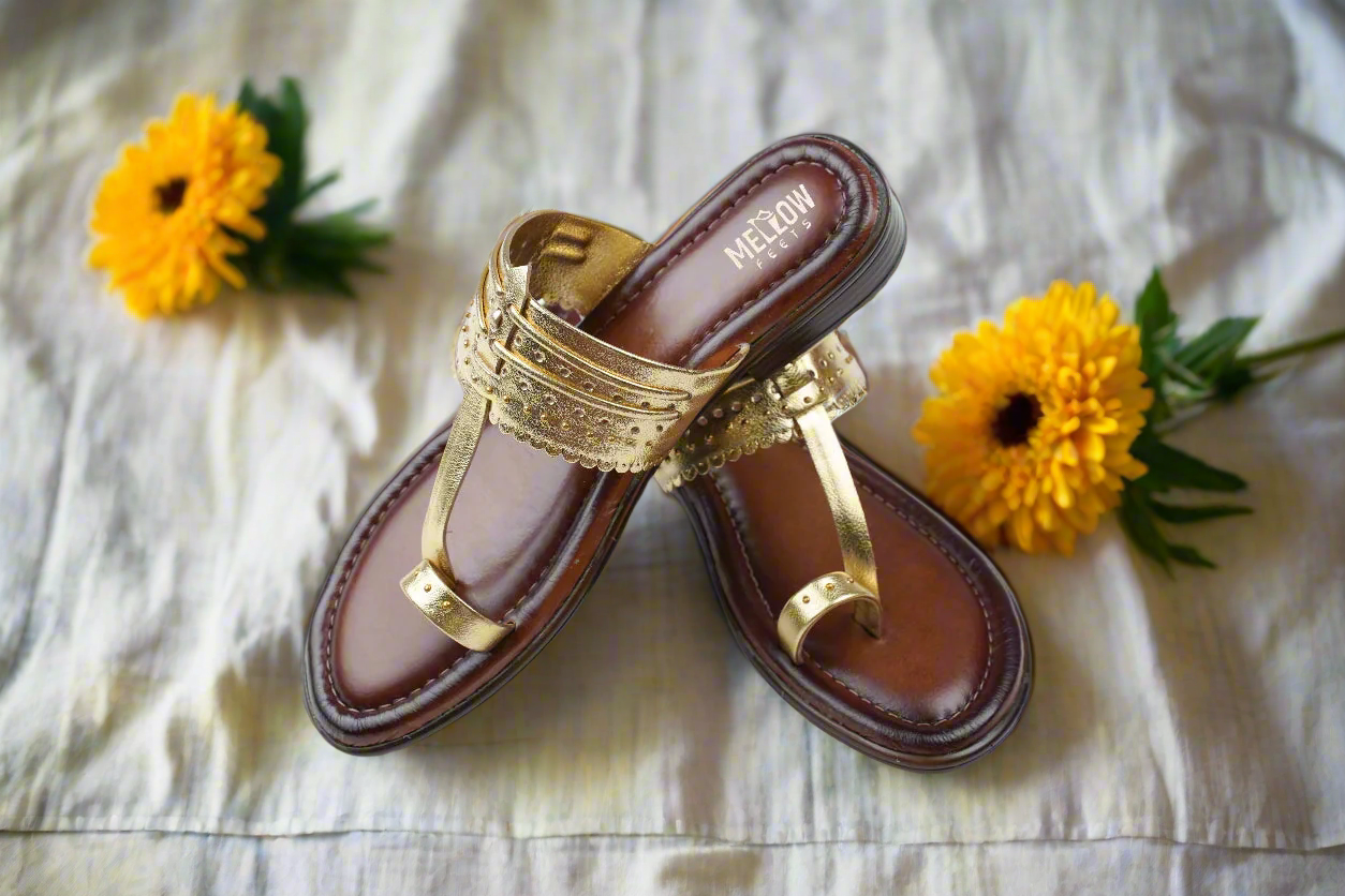 Brown sandal with gold straps on a light surface with flowers around