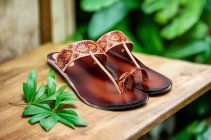 Pair of brown leather sandals with intricate designs on a wooden surface.