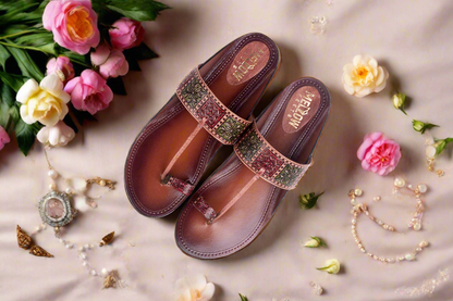 Pair of brown sandals with decorative straps on a light background with flowers and jewelry.