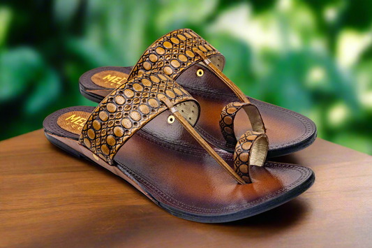 Pair of brown sandals with decorative straps on a wooden surface with a blurred green background