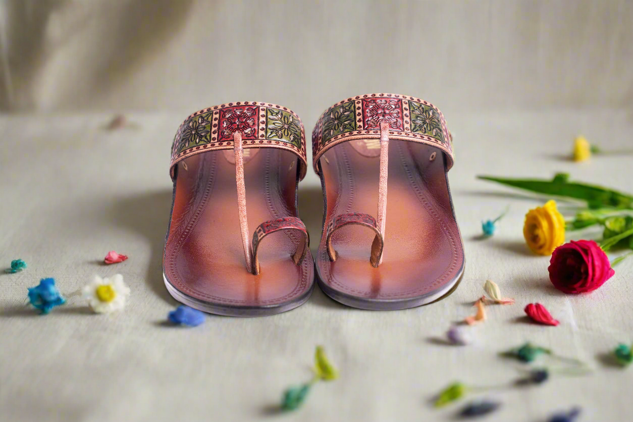 Pair of pink sandals with decorative straps on a light surface with small flowers around.