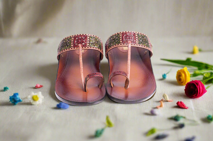 Pair of pink sandals with decorative straps on a light surface with small flowers around.