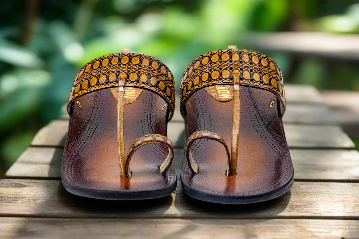 Pair of brown sandals with patterned straps on a wooden surface with a blurred green background